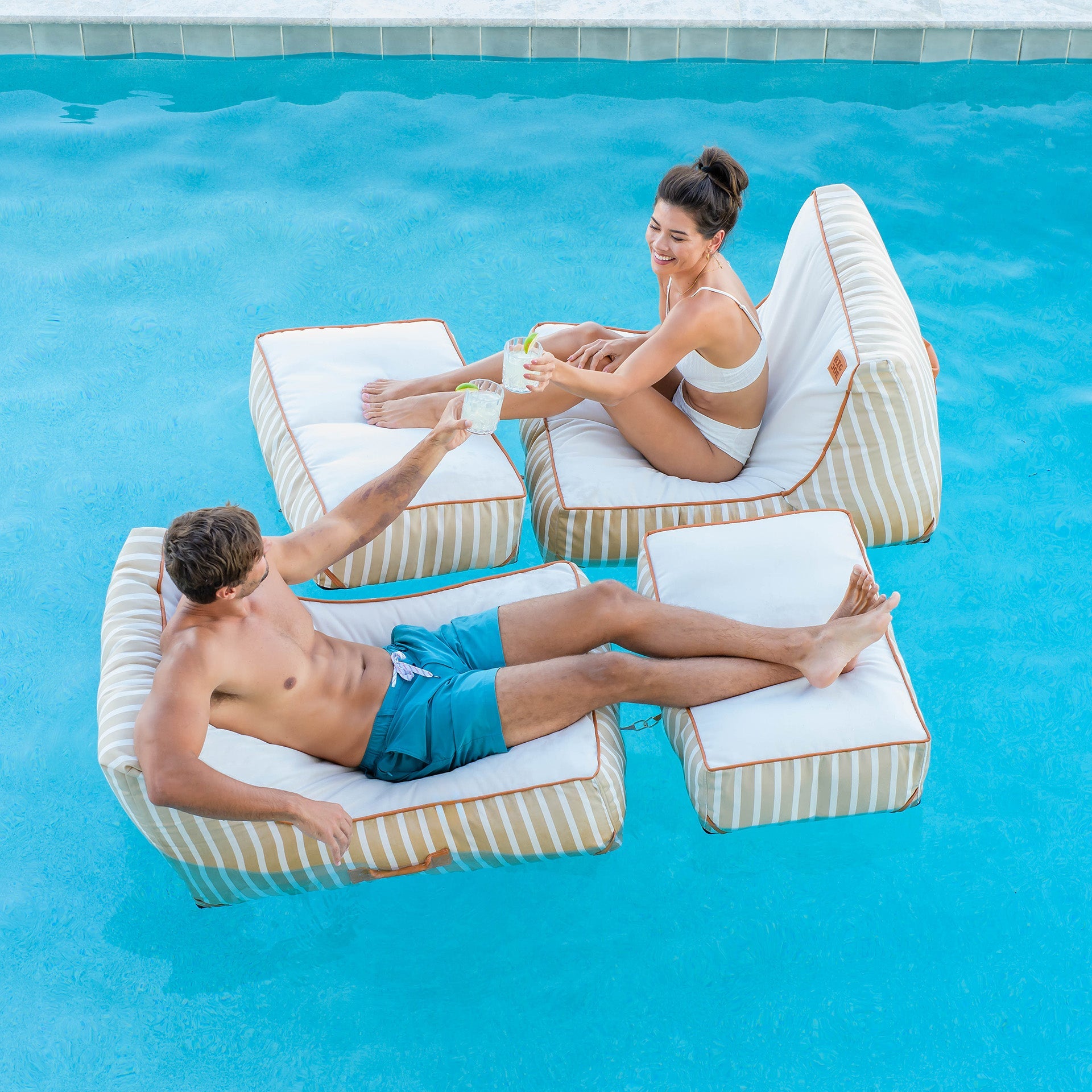 Two people relaxing on inflatable pool chairs in a pool.
