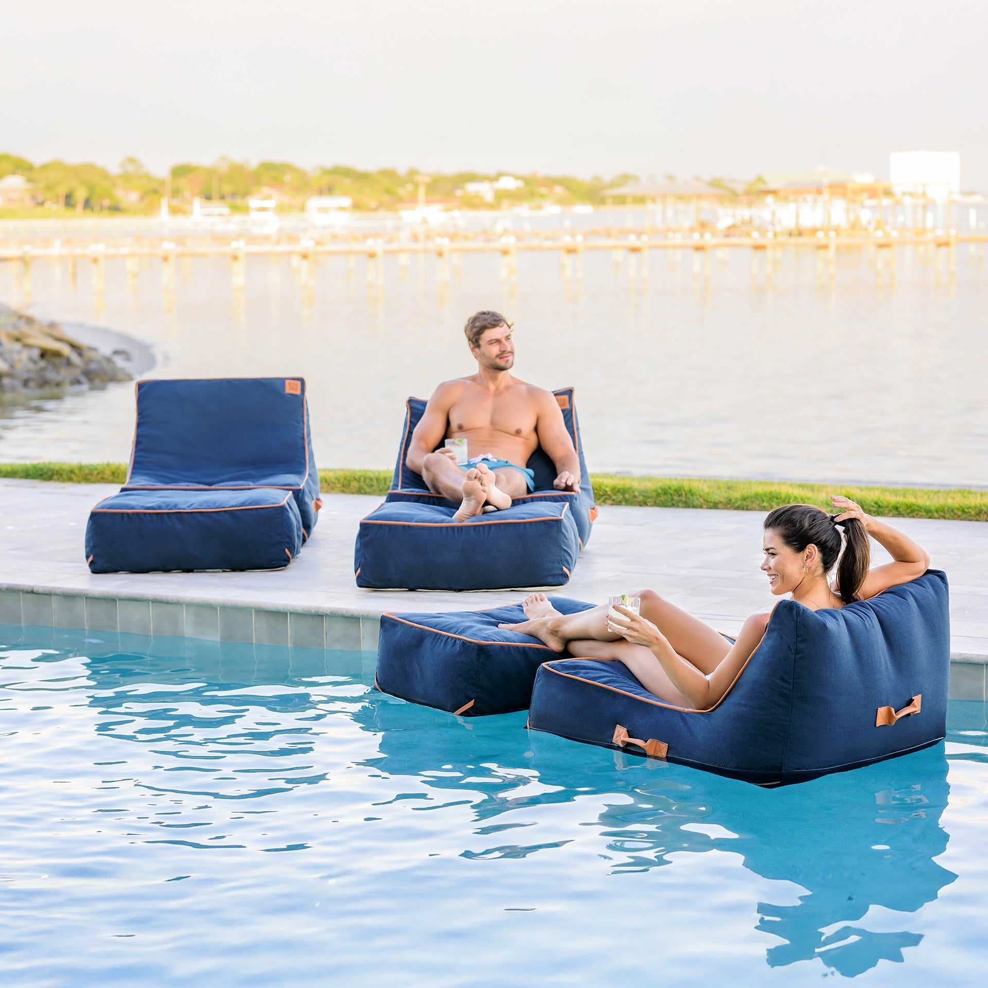 Two people relaxing on blue inflatable lounge chairs by a pool.
