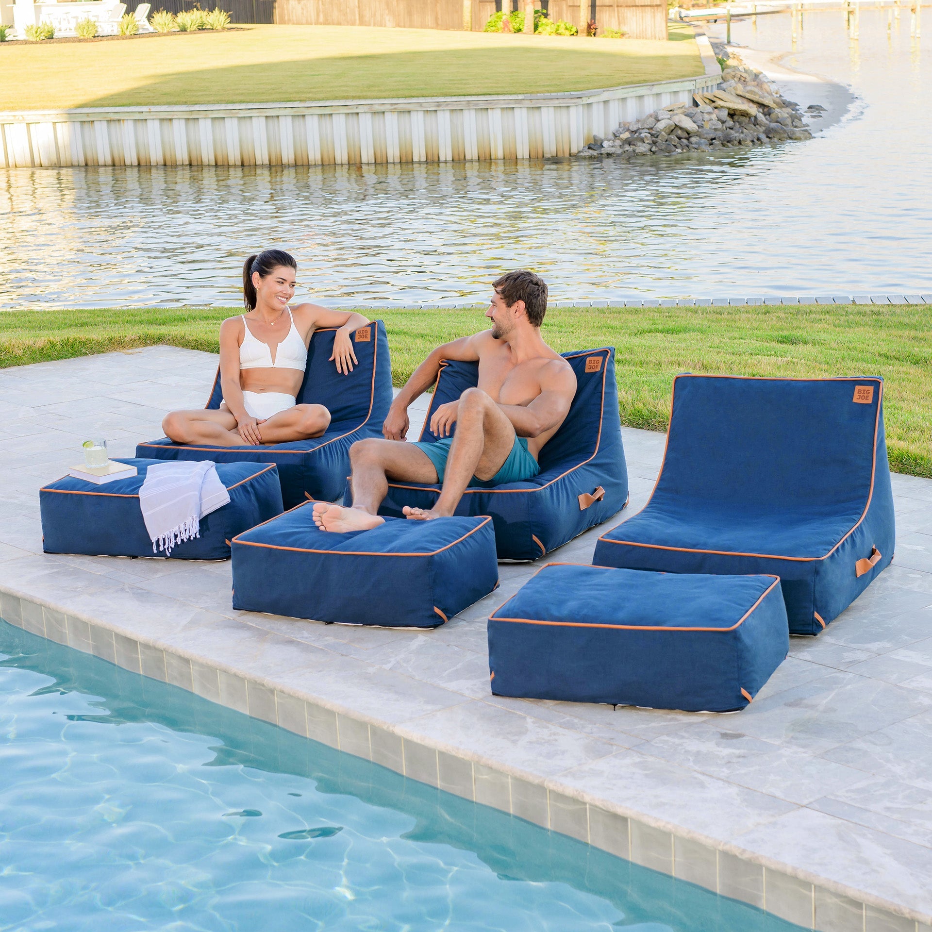 Two people sitting on blue lounge chairs by a poolside.