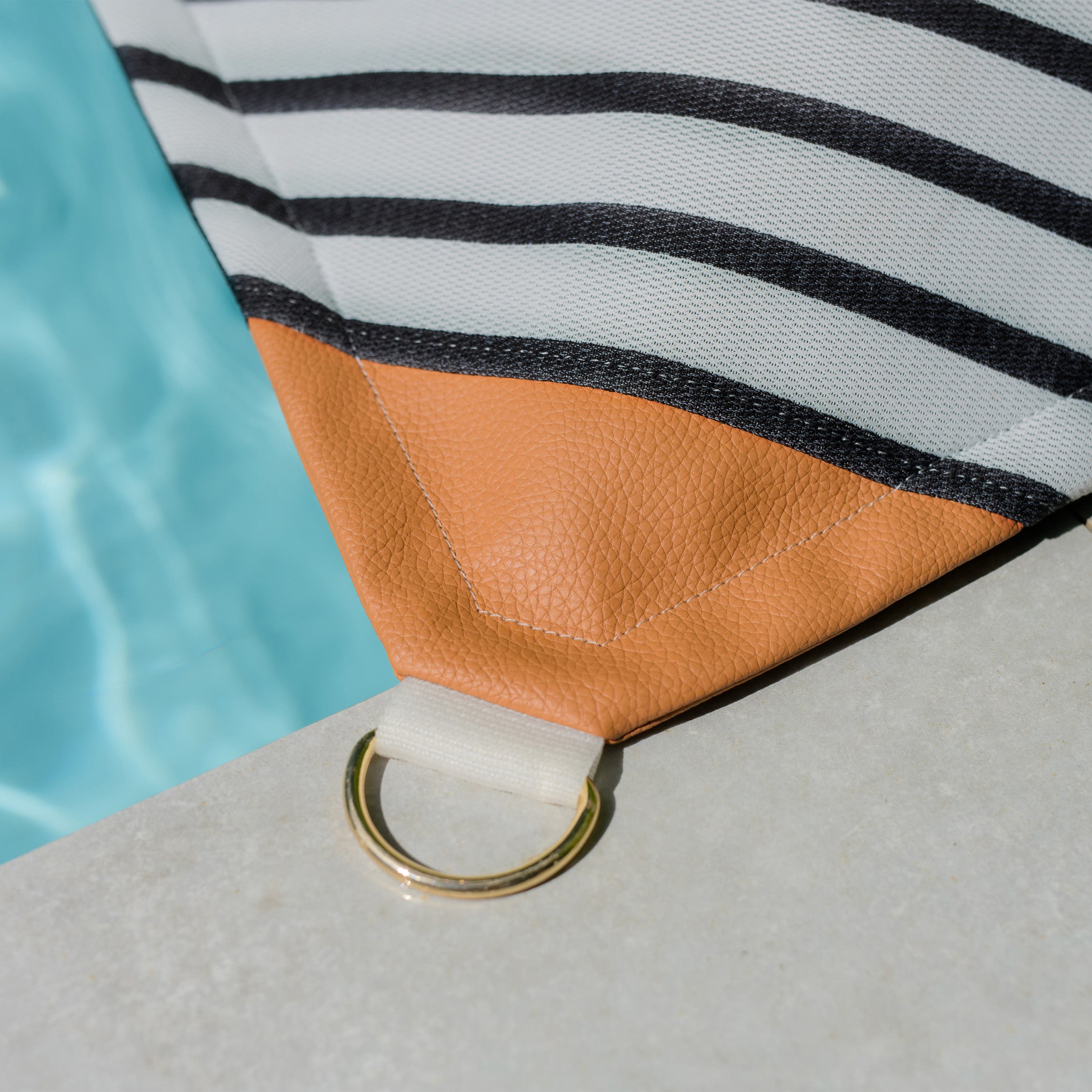 Close-up of a bag with a striped pattern and brown leather patch by a pool.