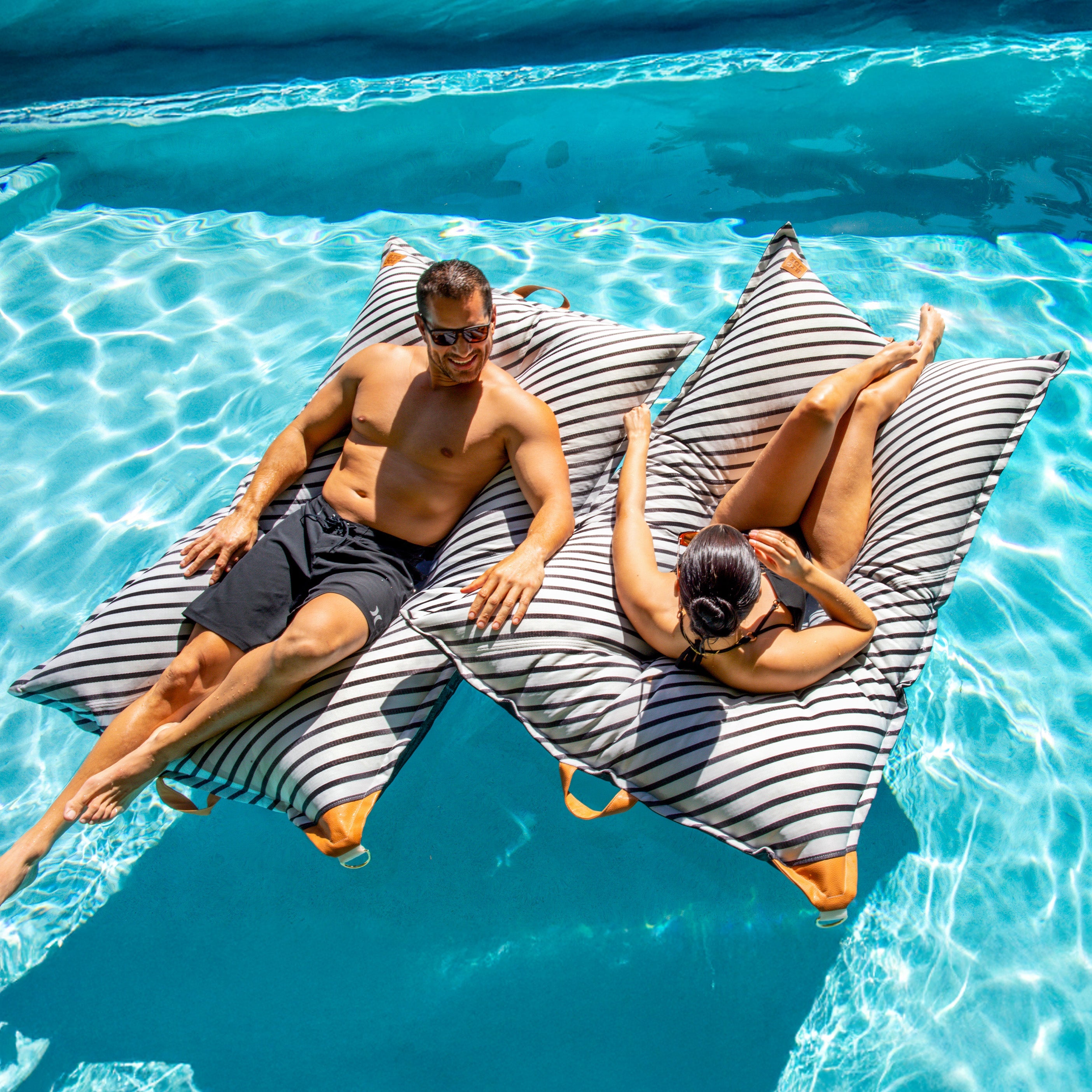 Two people lounging on striped bean bags in a pool