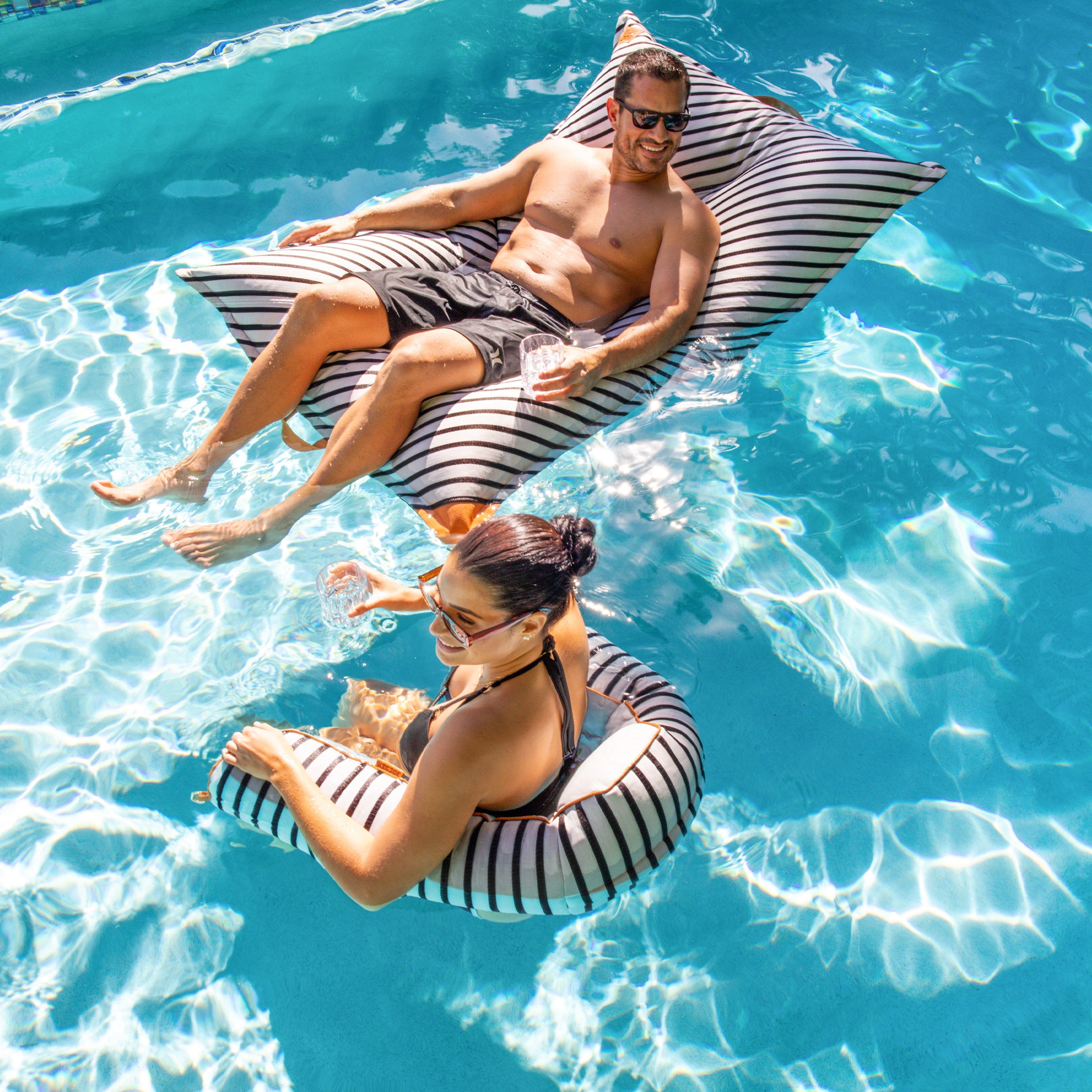 Two people lounging on striped inflatable chairs in a pool.