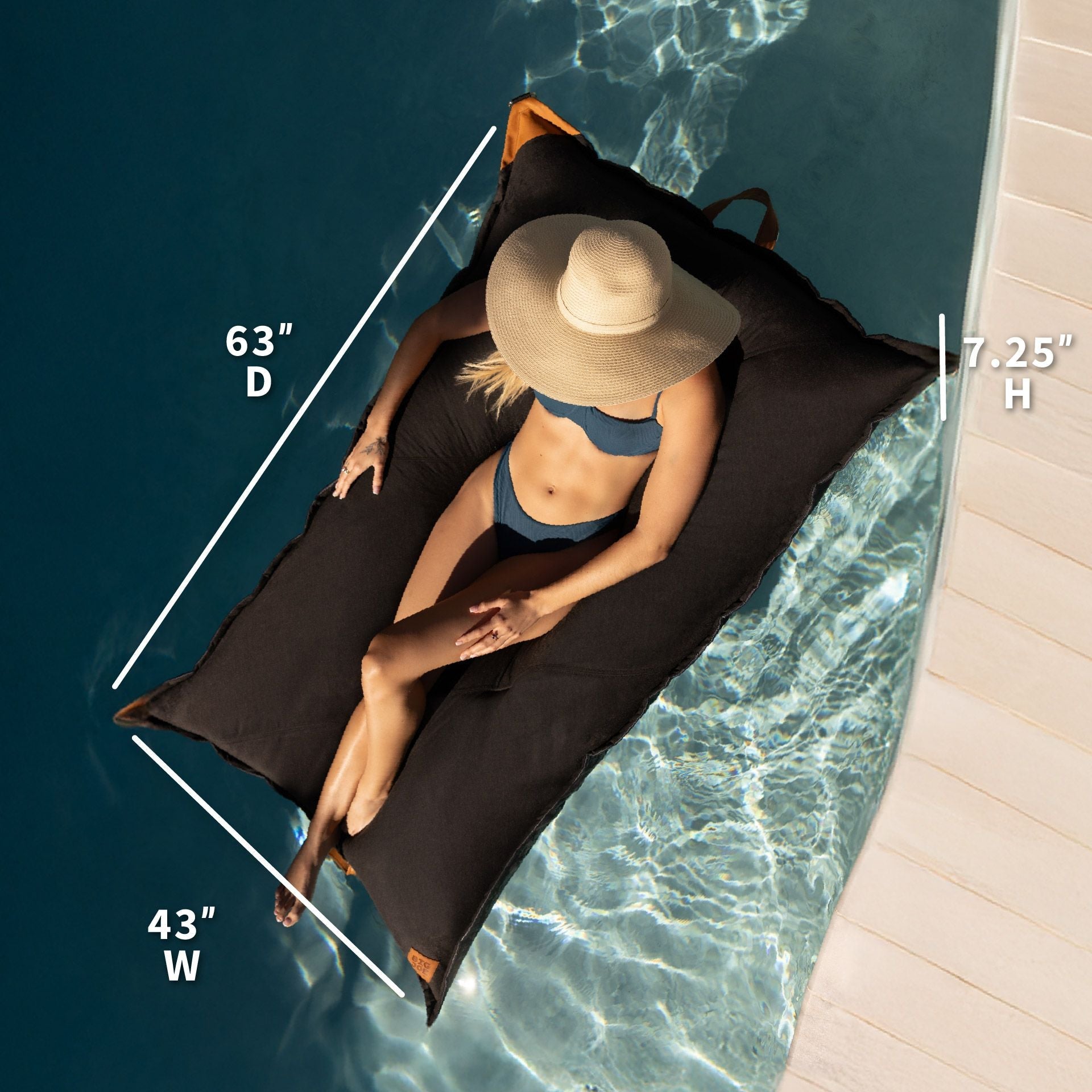 Person lounging on a large black bean bag by a pool with measurements displayed.