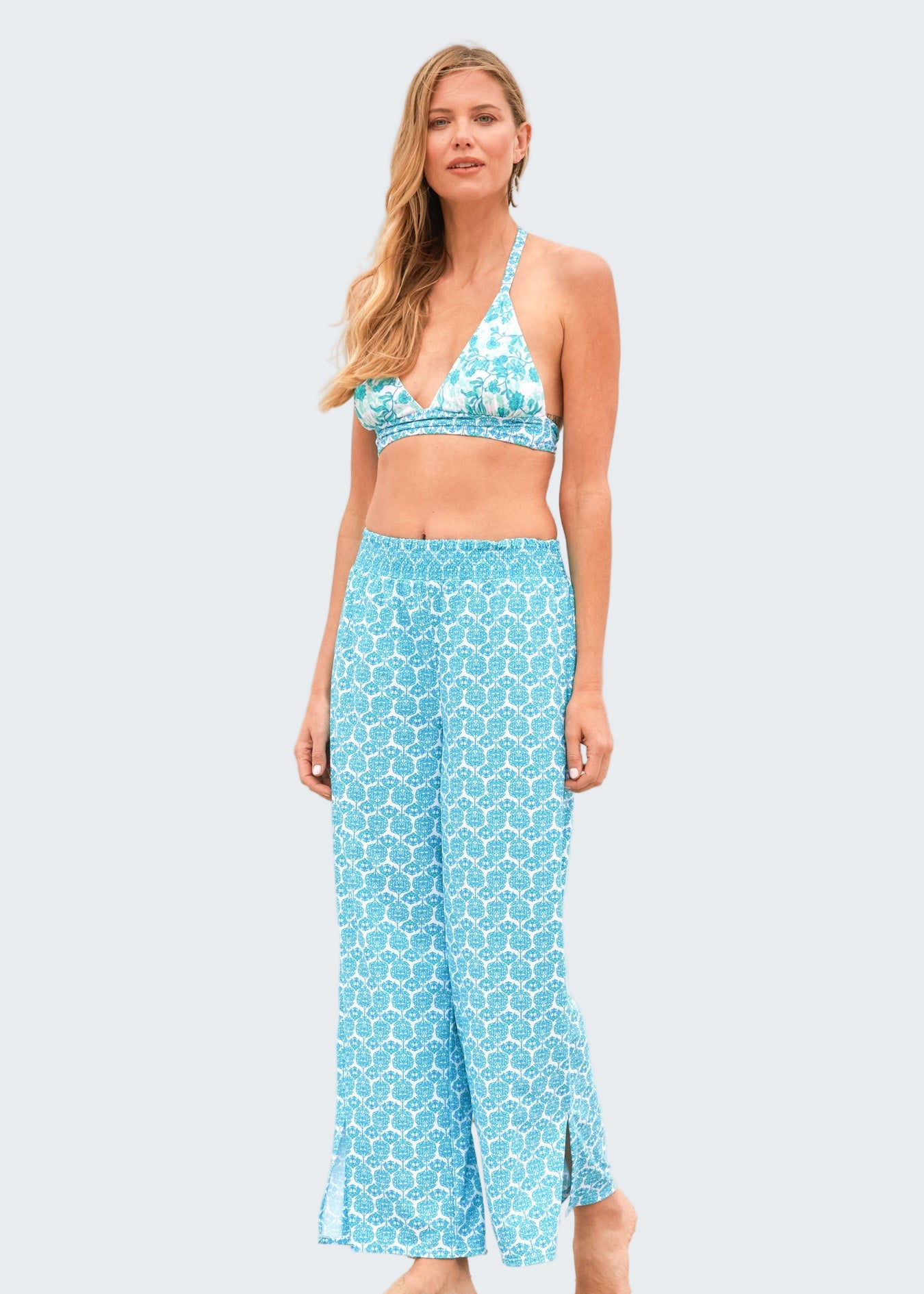 Woman wearing a blue patterned bikini and pants on a beach