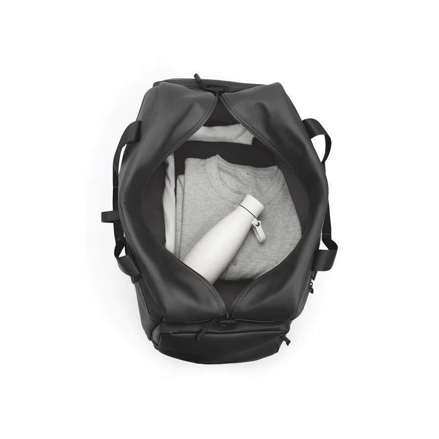 Black backpack with gray shirt and white bottle inside on a white background