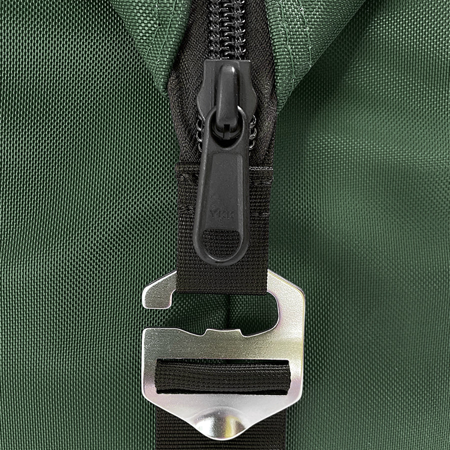 Close-up of a green bag with a black zipper and metal buckle on a matching green background.