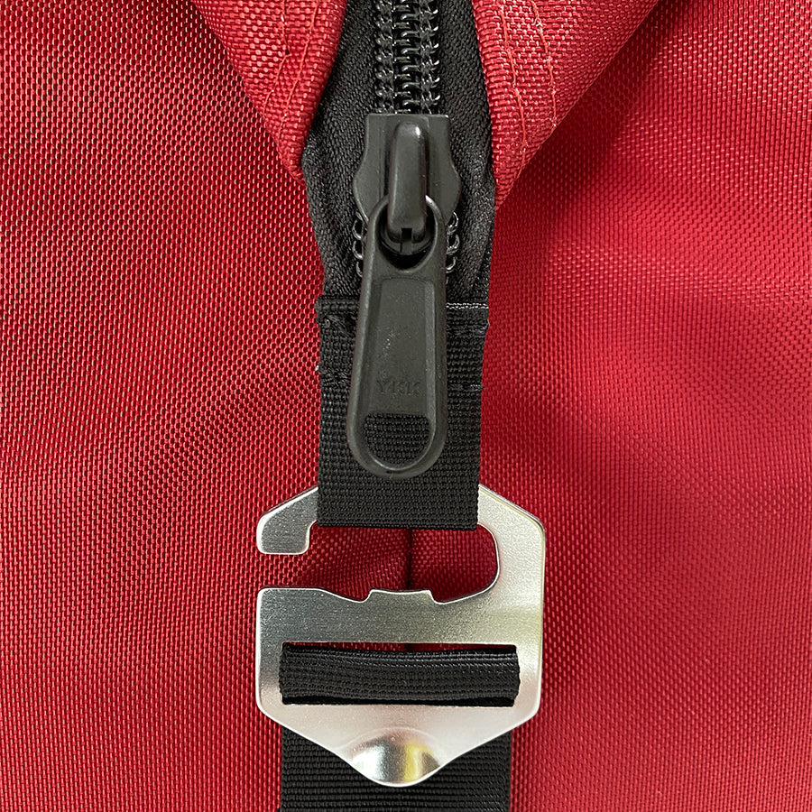 Close-up of a red bag with a black zipper and silver buckle on a red background