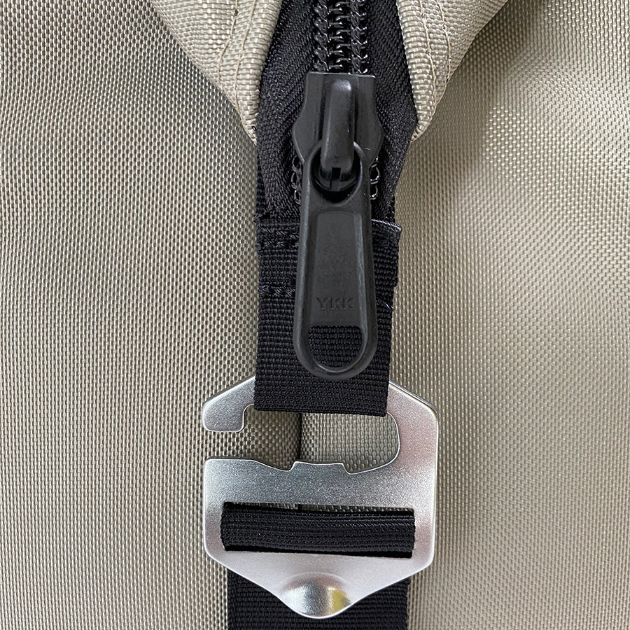 Close-up of a beige bag with a black zipper and metal buckle on a beige background