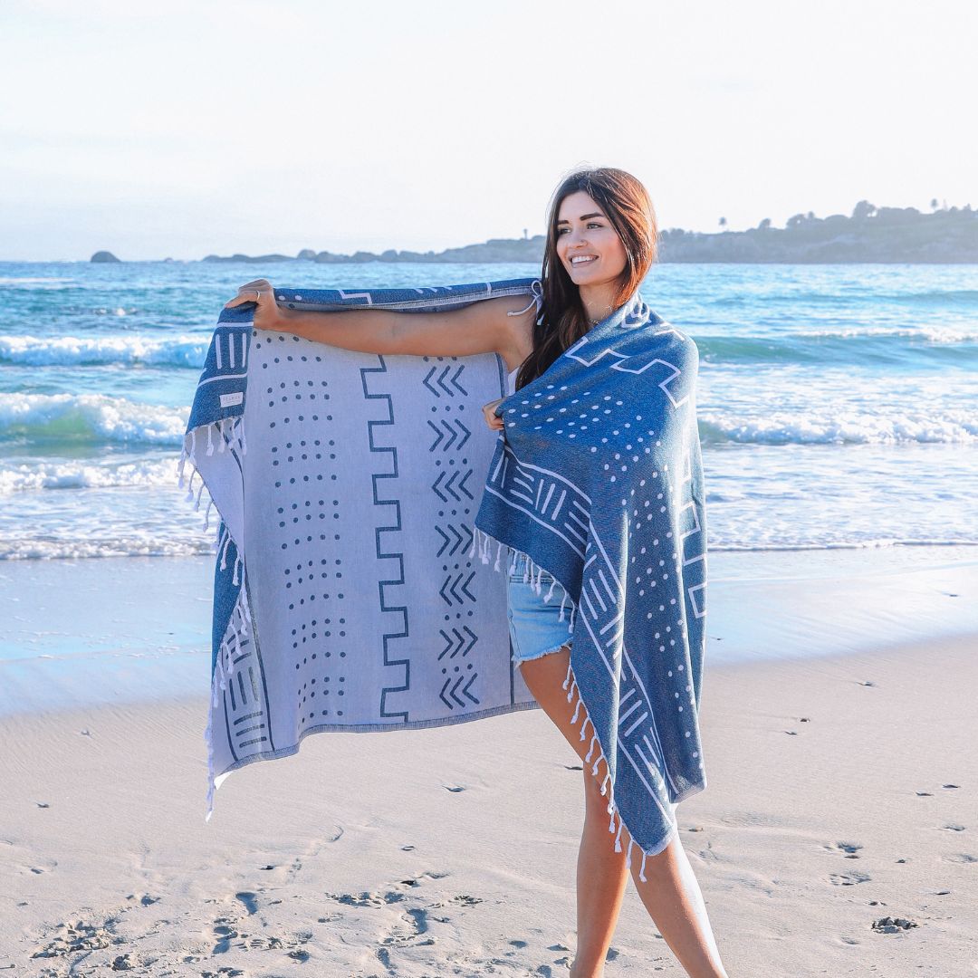 Woman holding a blue and white patterned towel on a beach