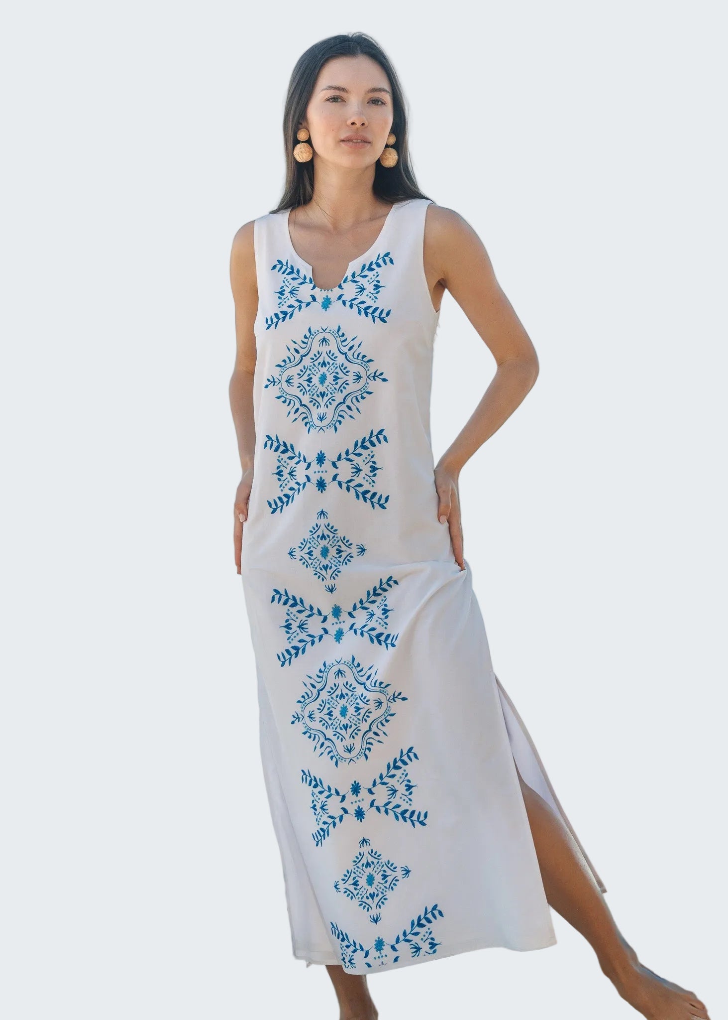 Woman wearing a white dress with blue floral patterns on a beach.