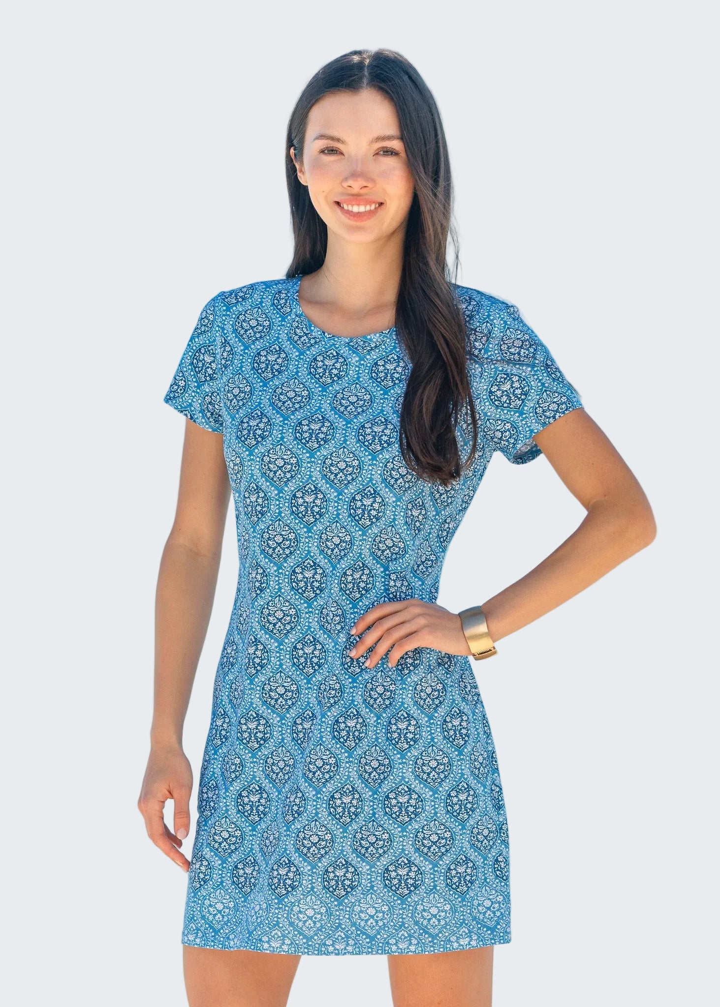 Woman wearing a blue patterned dress standing on a beach with ocean in the background