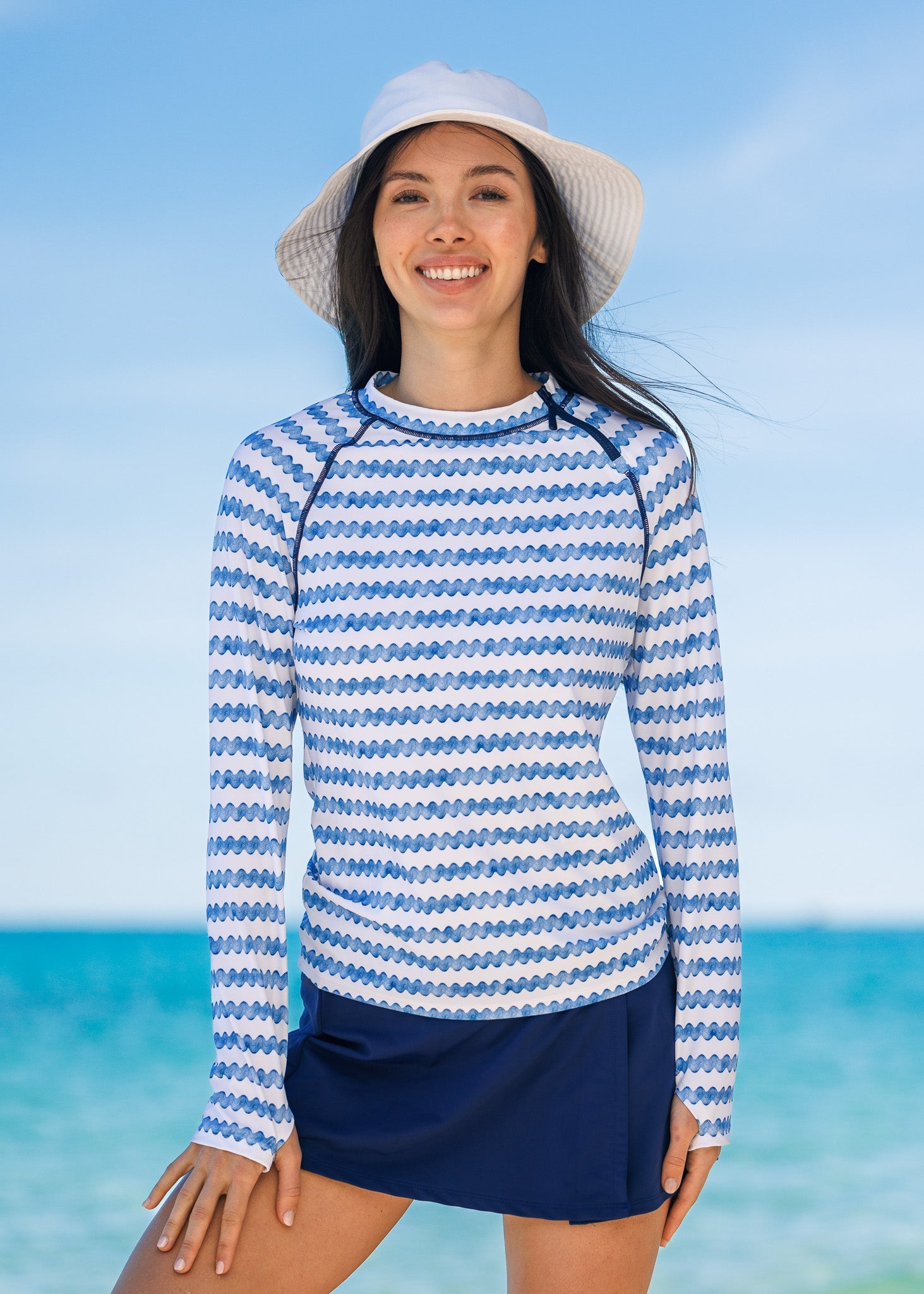 Woman wearing a blue and white striped long-sleeve shirt and navy skirt on a beach.