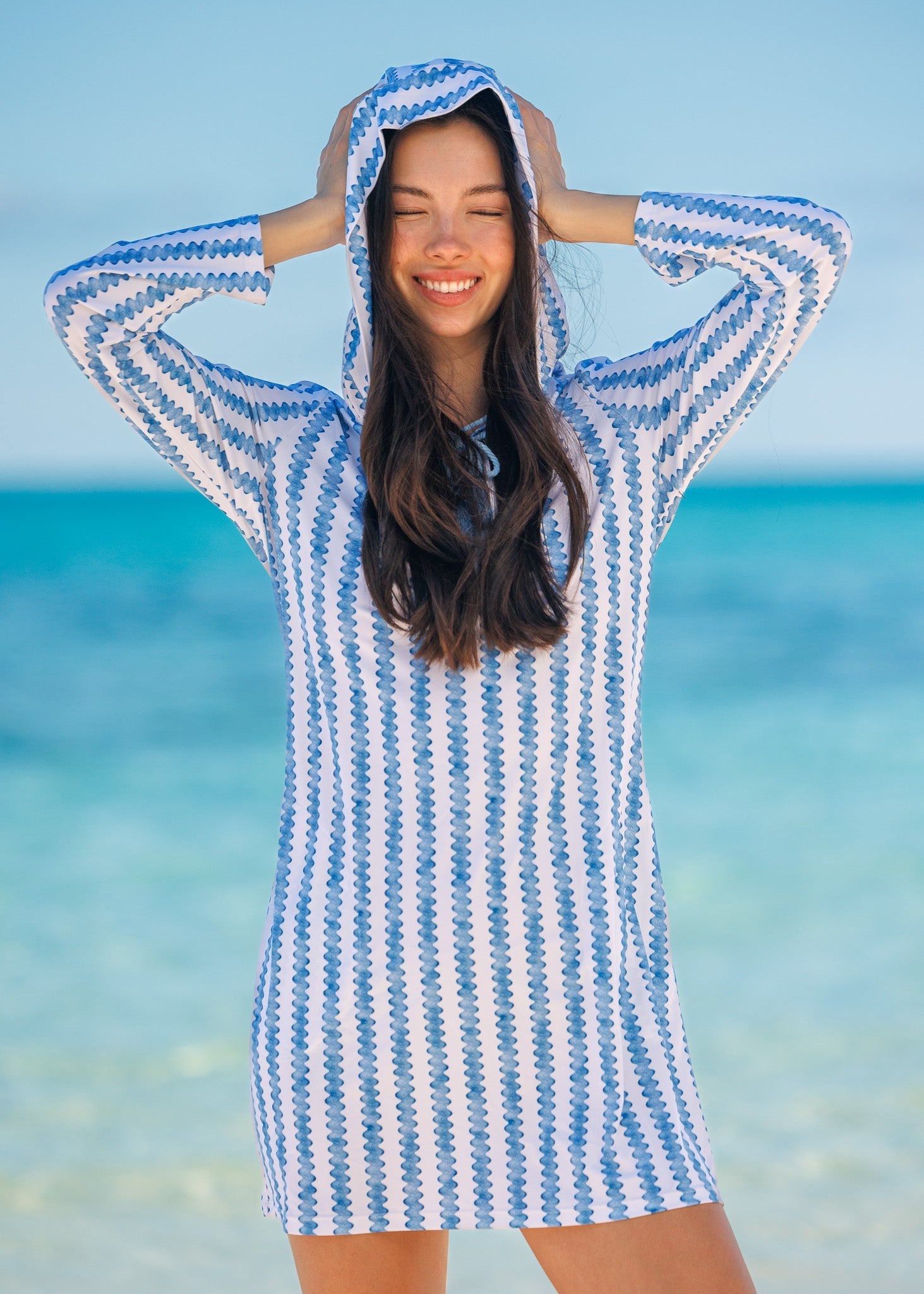 Woman wearing a blue and white striped hooded towel on a beach