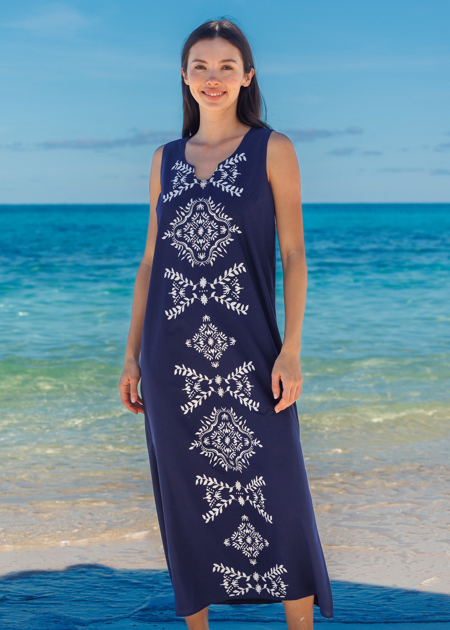 Woman wearing a navy dress with white patterns standing on a beach.