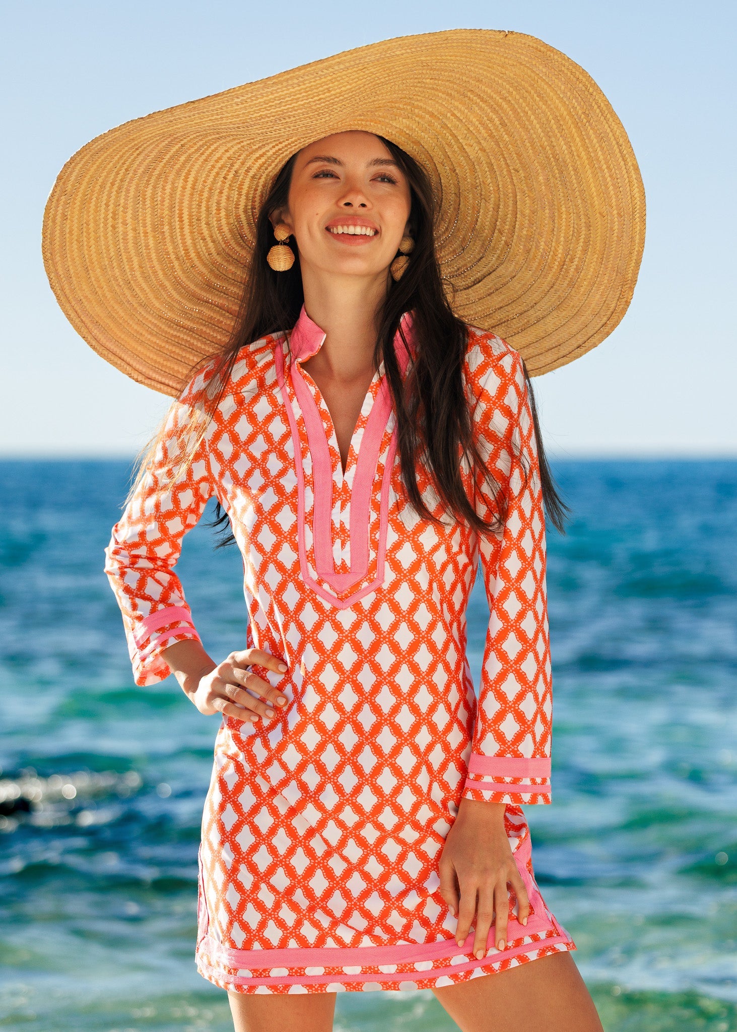 Woman wearing a colorful dress and large straw hat by the ocean