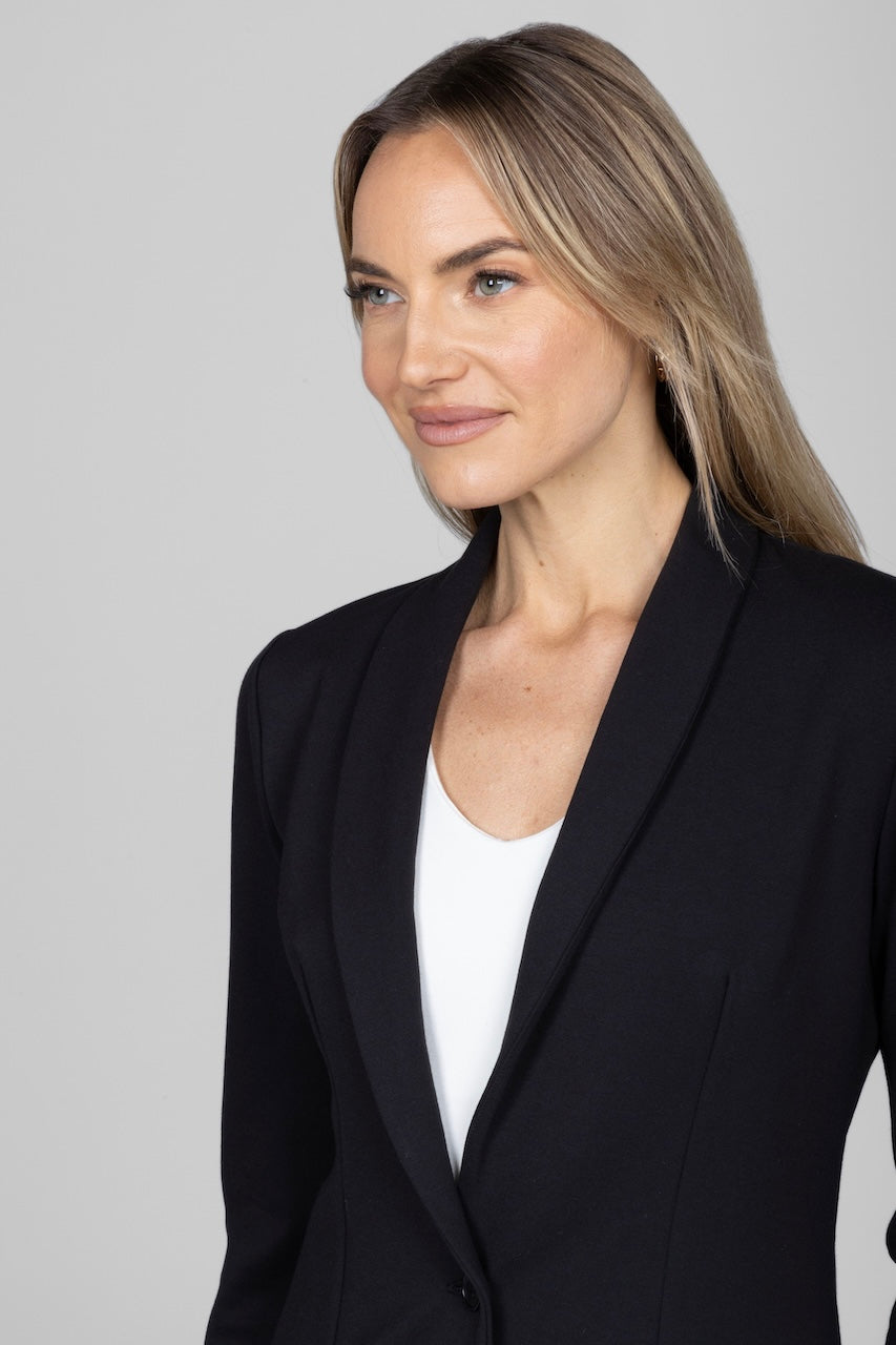 Woman wearing a black blazer over a white top against a plain background
