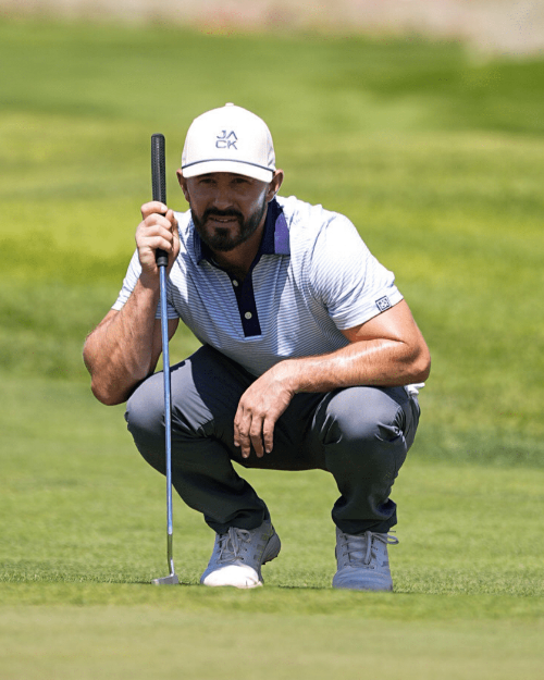 Golfer crouching on a green golf course holding a club.