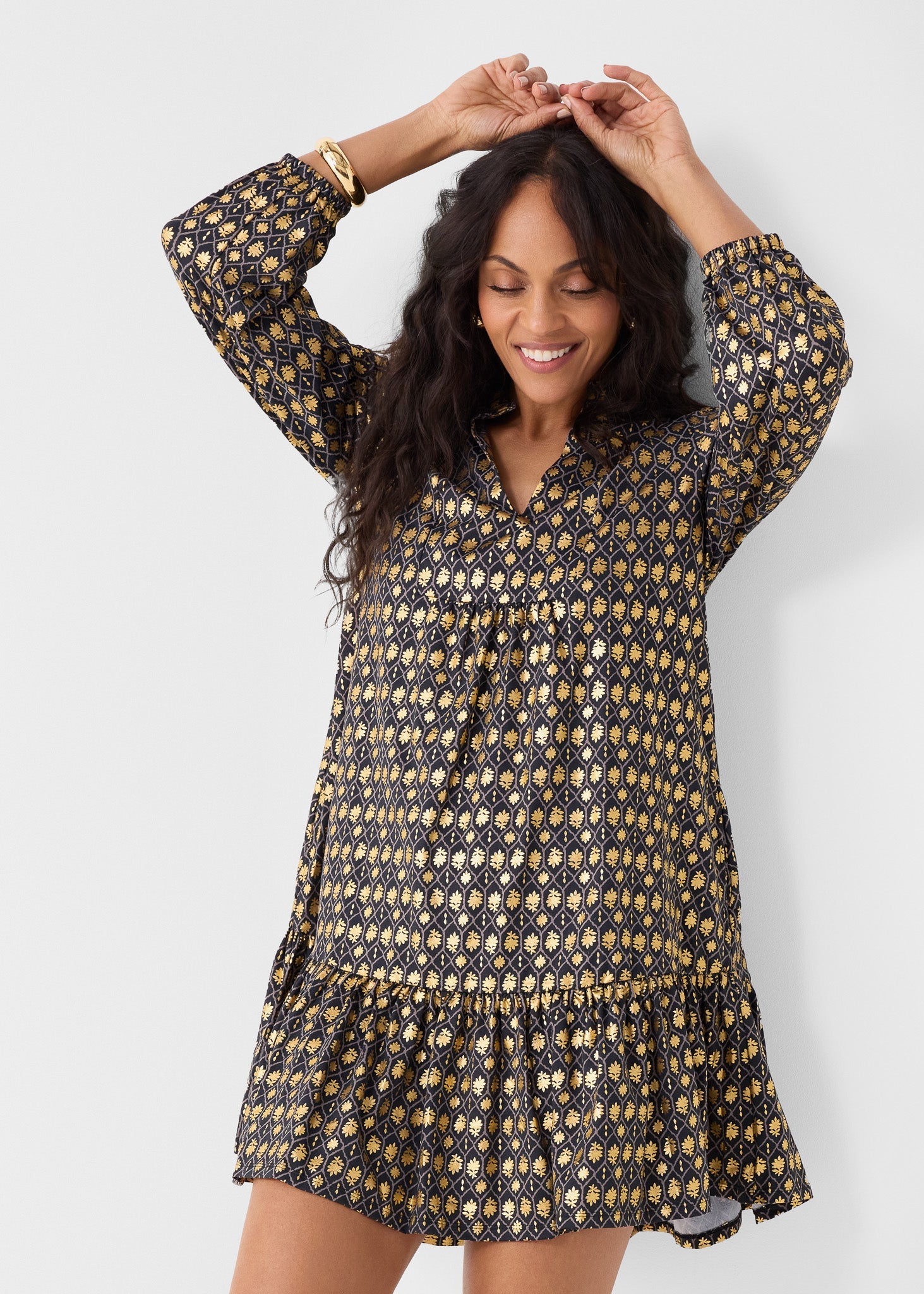 Woman wearing a black and gold patterned dress against a white background