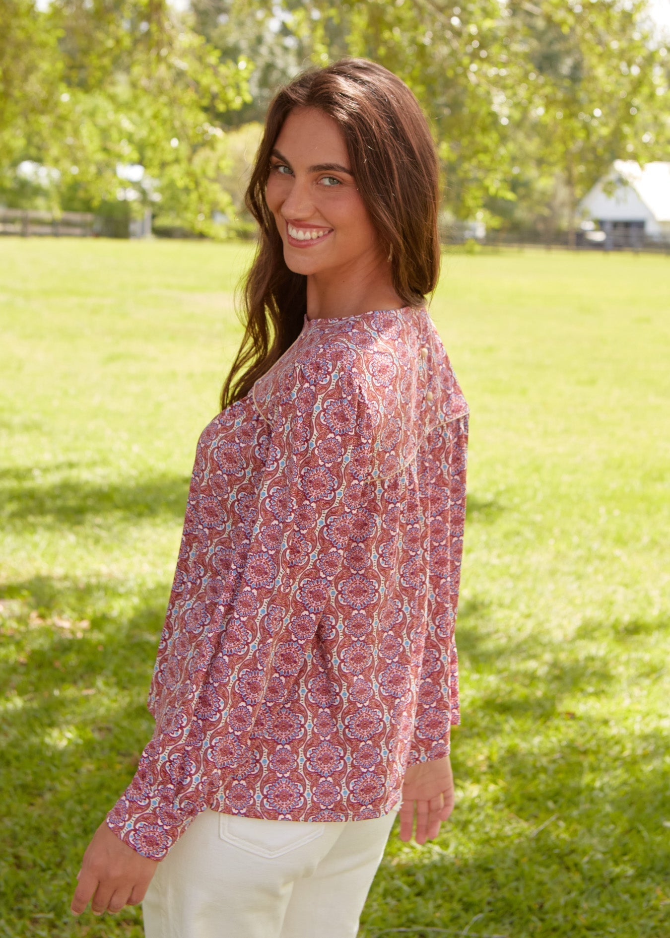 Woman wearing a patterned blouse standing in a grassy field