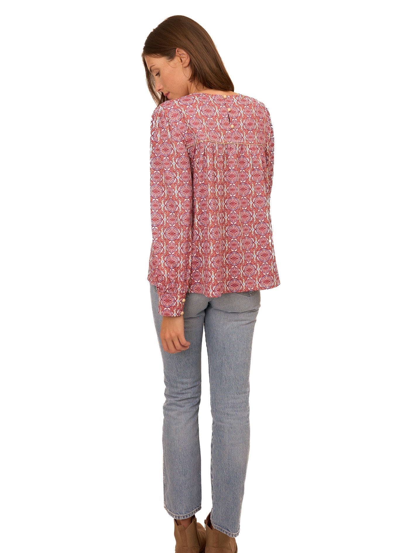 Person wearing a red patterned blouse and gray pants on a white background