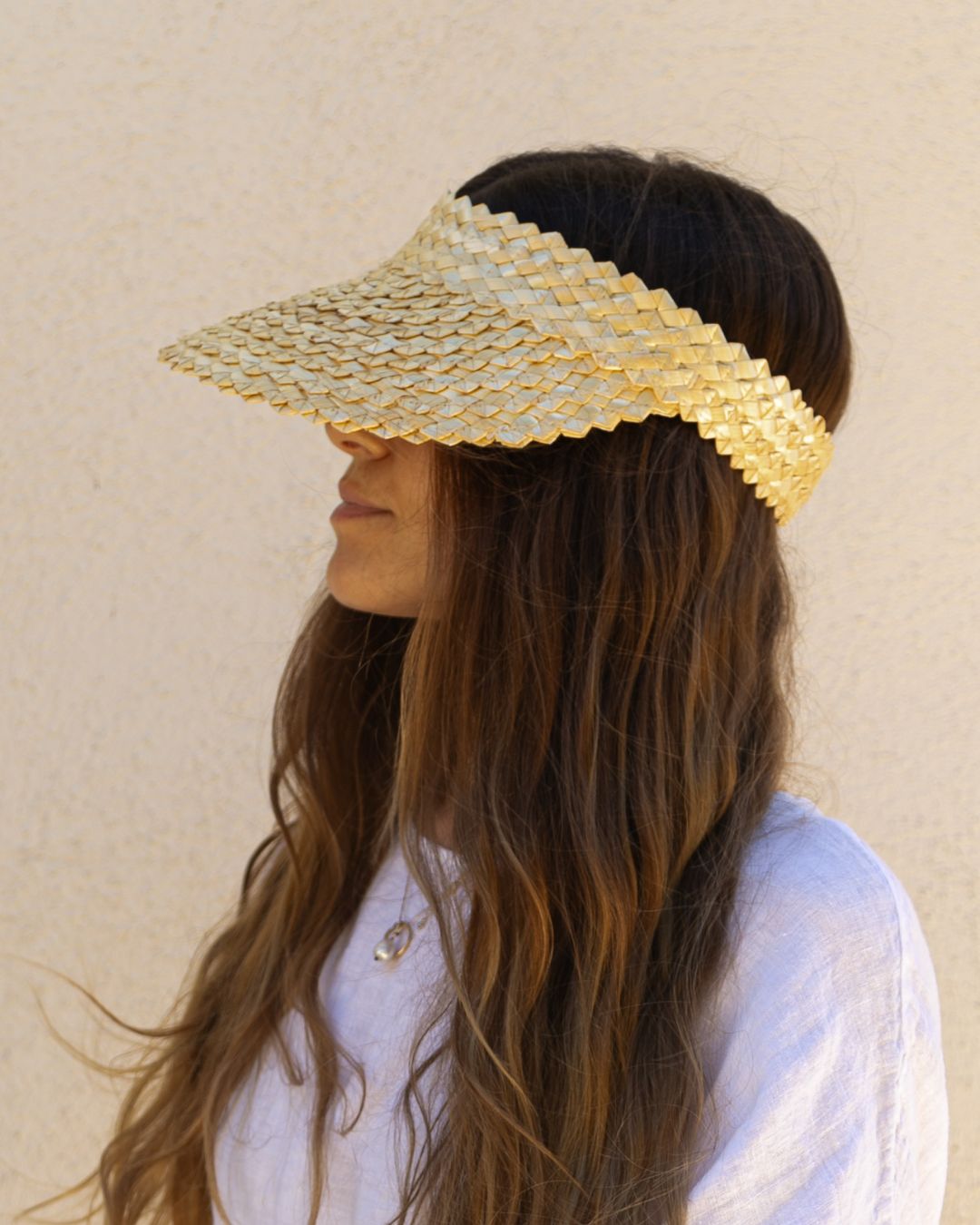 Woman wearing a gold visor against a beige background