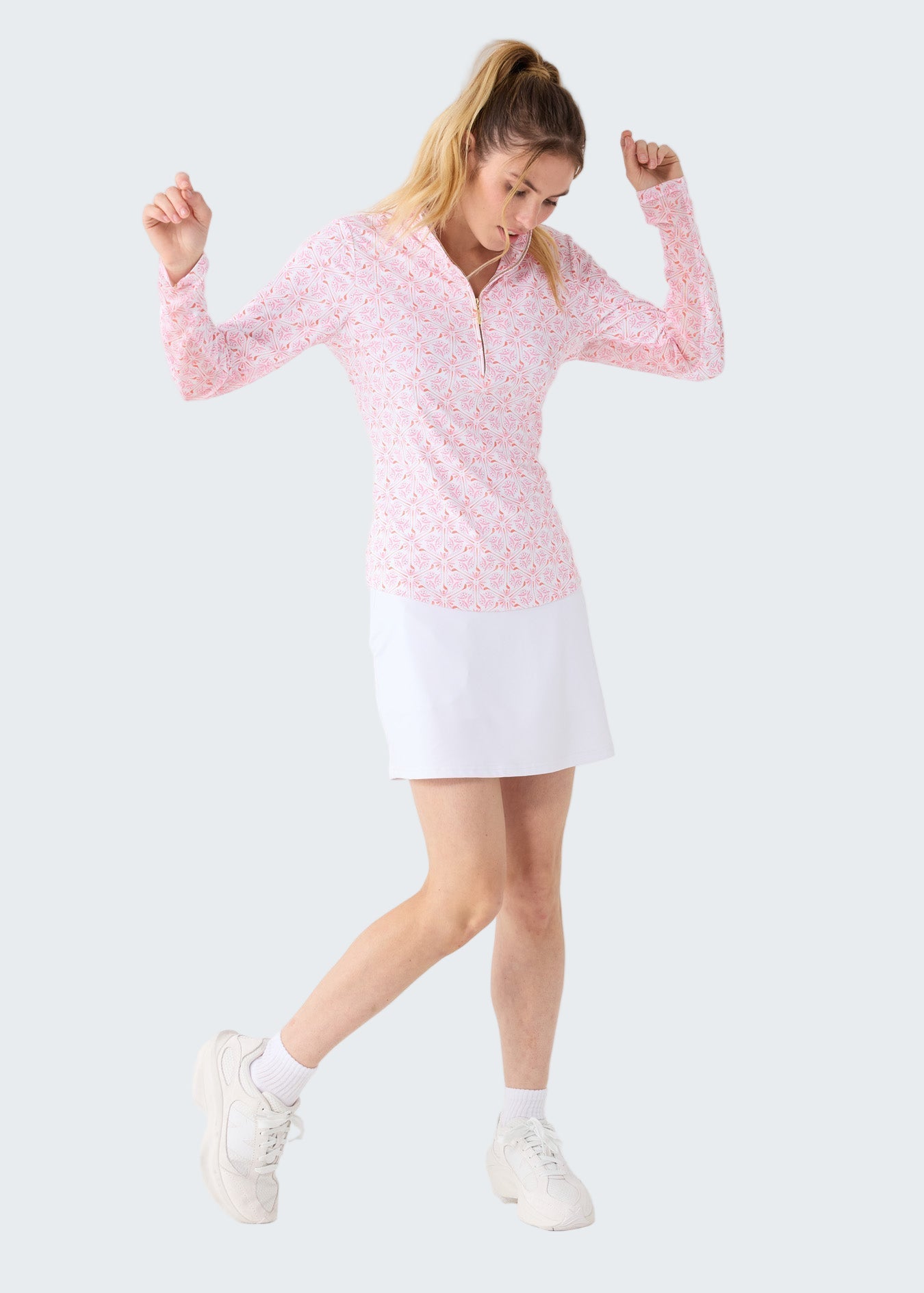 Woman wearing a pink long-sleeve top and white skirt on a white background
