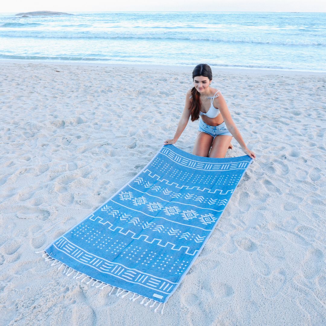 Woman on a beach holding a blue and white patterned towel