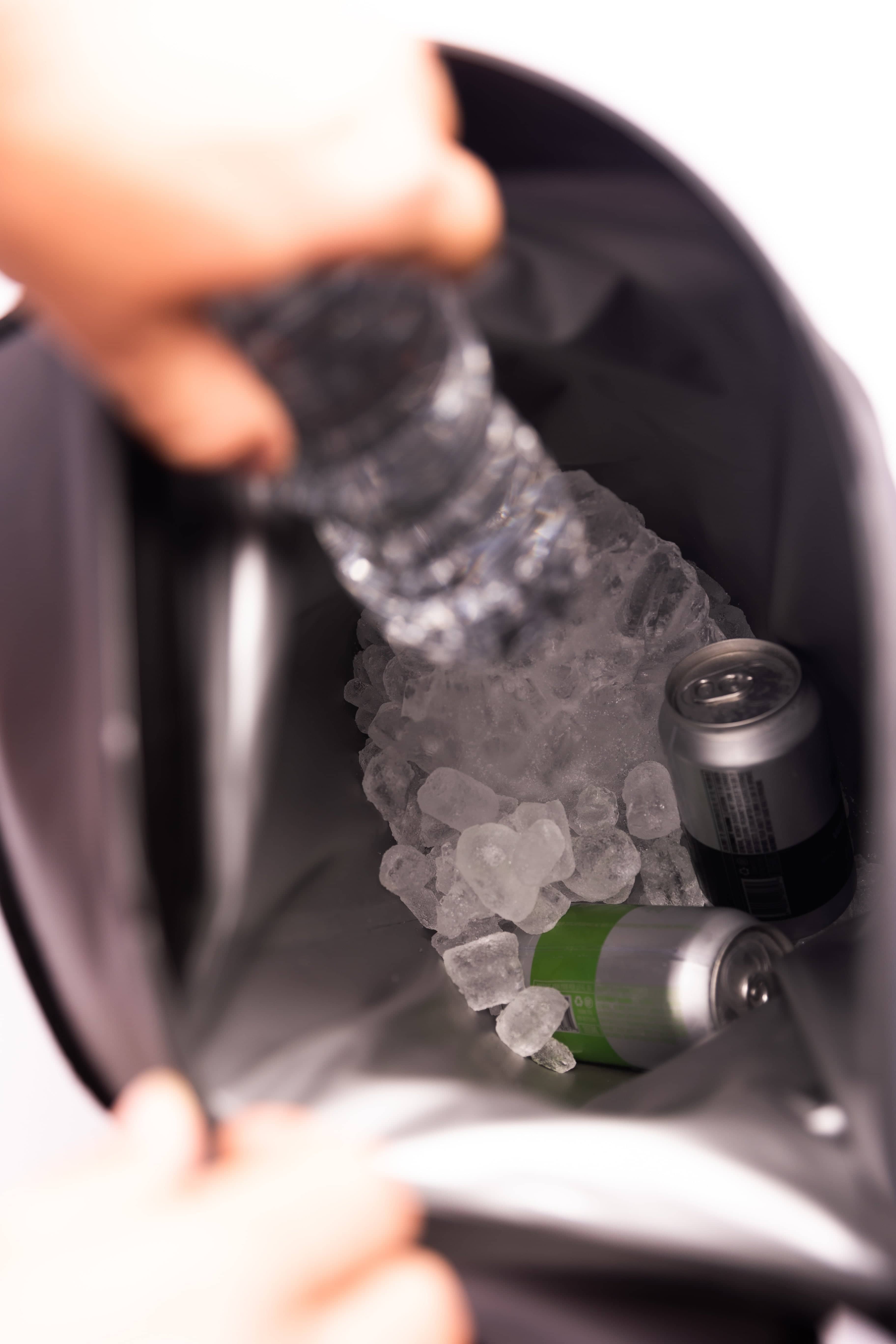 Person filling a water bottle with ice cubes from a freezer.