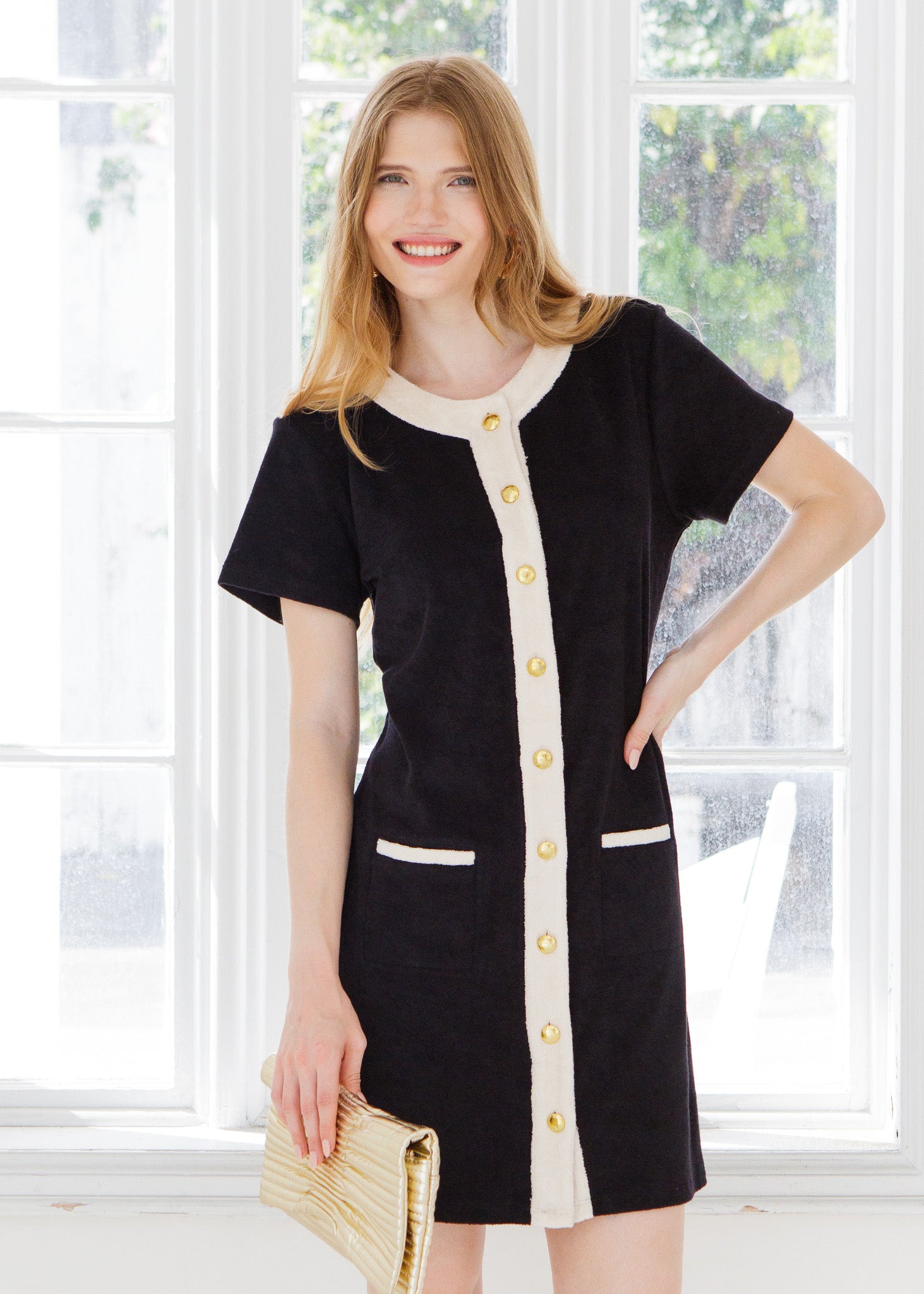 Woman wearing a black dress with gold buttons in a bright room.