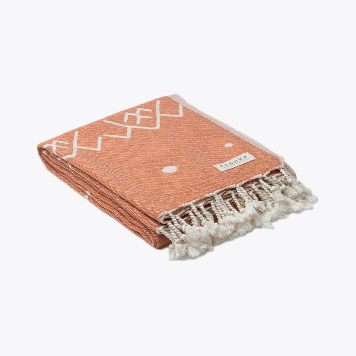 Folded peach-colored towel with white patterns and fringes on a white background
