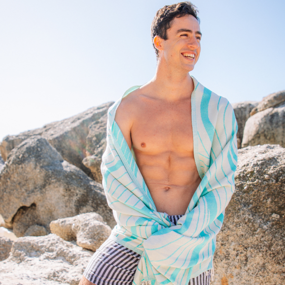 Man wrapped in a light blue towel with white patterns, standing on rocky terrain.
