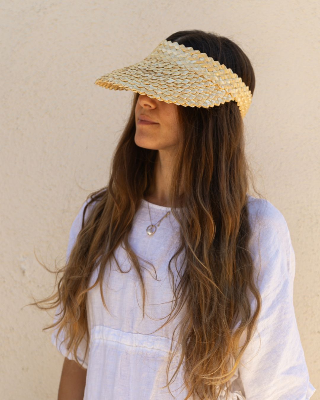 Woman wearing a straw visor against a beige background