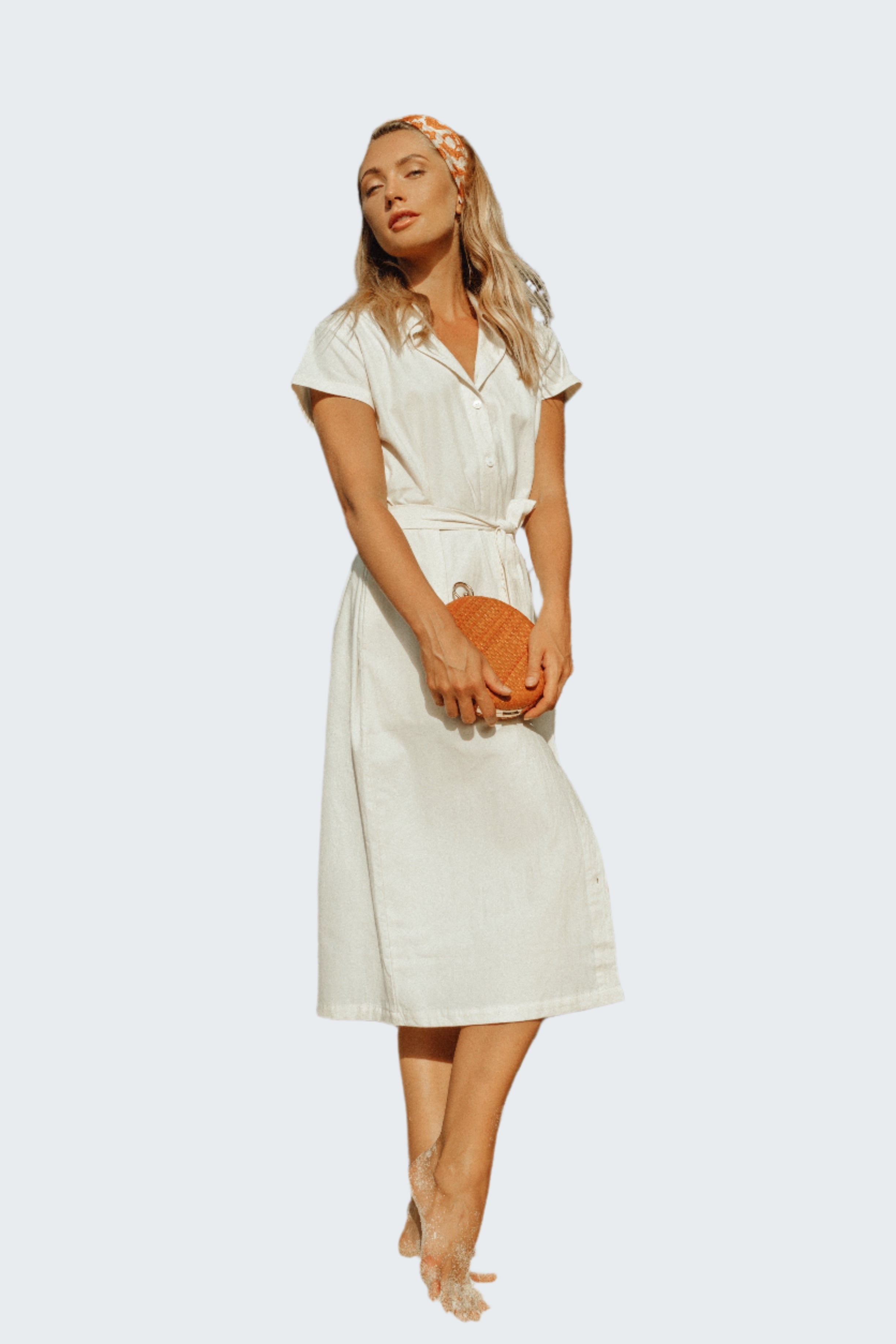 Woman in a white dress standing against a rocky wall.