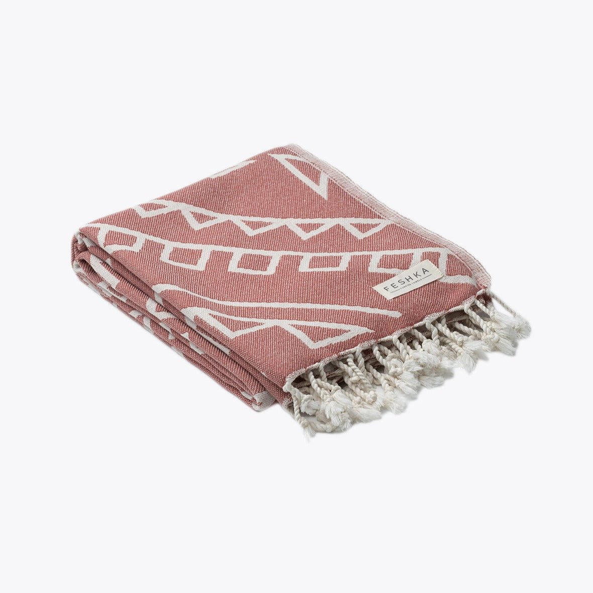 Folded pink towel with white geometric patterns and fringes on a white background