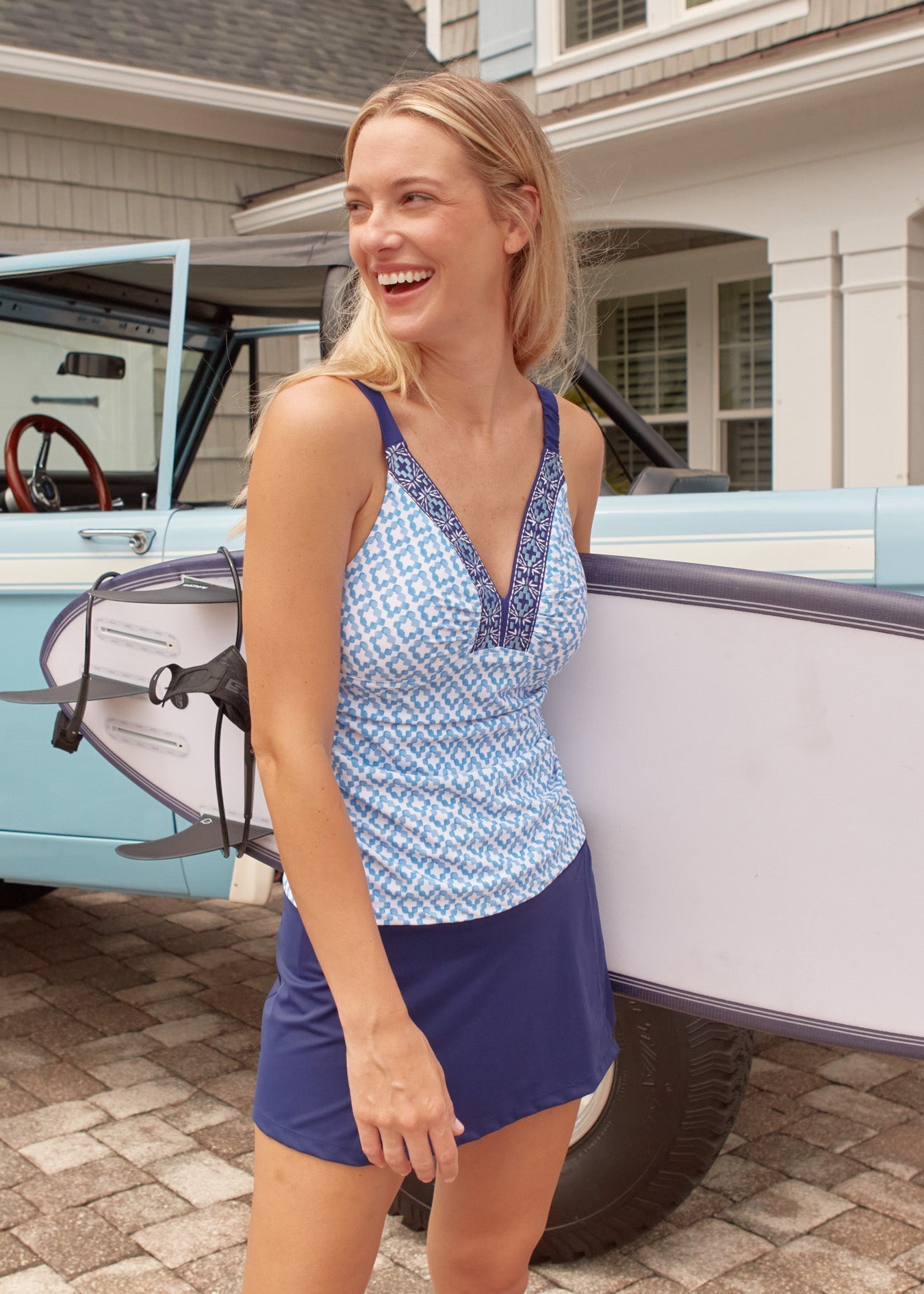 Woman in a blue and white patterned top and shorts standing next to a vintage car.