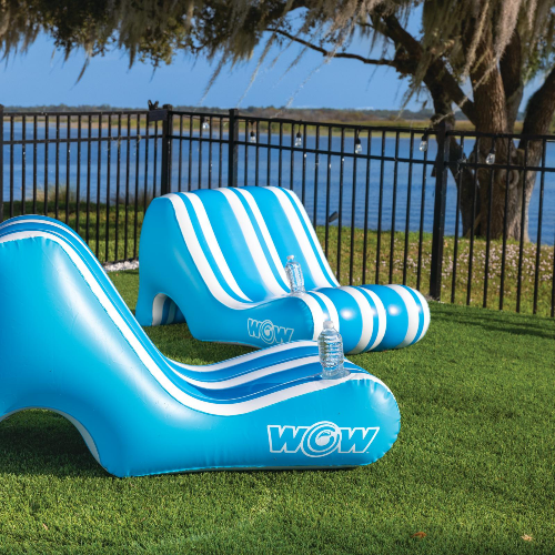 Inflatable blue and white striped slide with 'WOW' branding on a grassy area by a body of water.