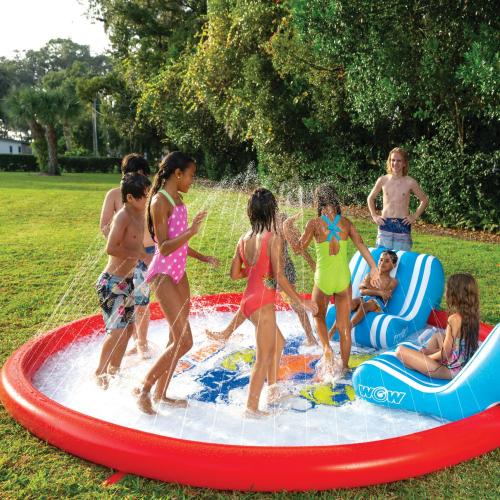 Children playing in an inflatable water park on a grassy area with trees in the background.