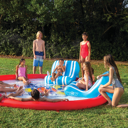 Children playing on an inflatable water park in a grassy area with trees in the background.