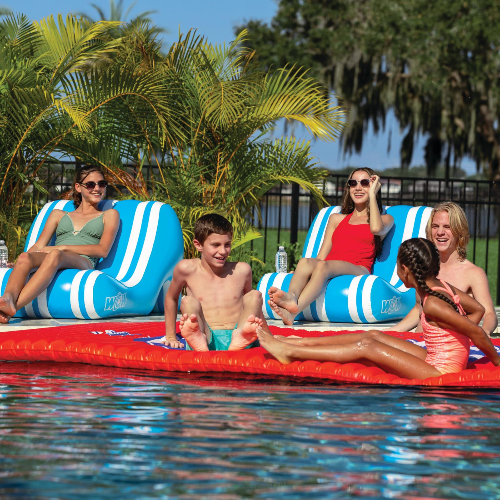 People relaxing on inflatable lounge chairs in a pool with palm trees in the background