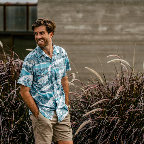 Man wearing a patterned shirt standing among tall grasses.