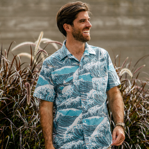 Man wearing a blue patterned shirt standing among tall grasses.