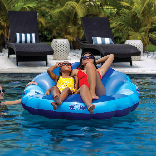 Two women on a blue inflatable pool float with 'WOW' branding in a pool setting.