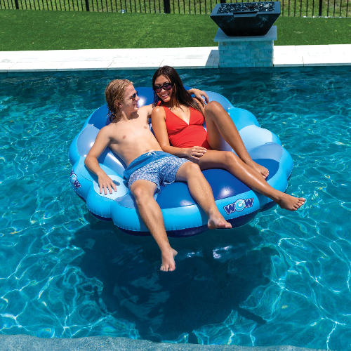 Two people relaxing on a blue inflatable pool float in a swimming pool.