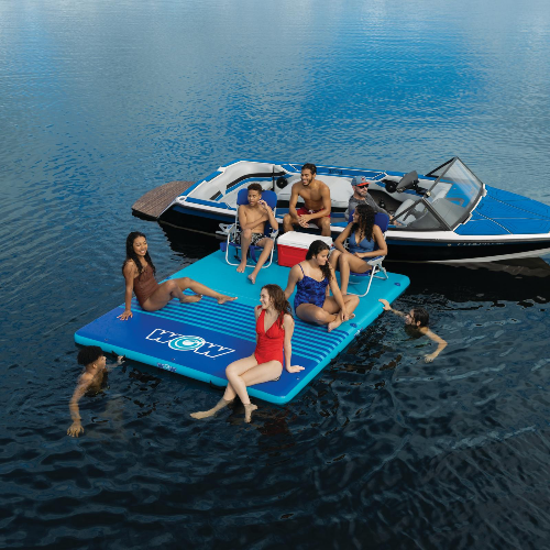 Group of people on a blue inflatable platform in the water with a boat in the background.