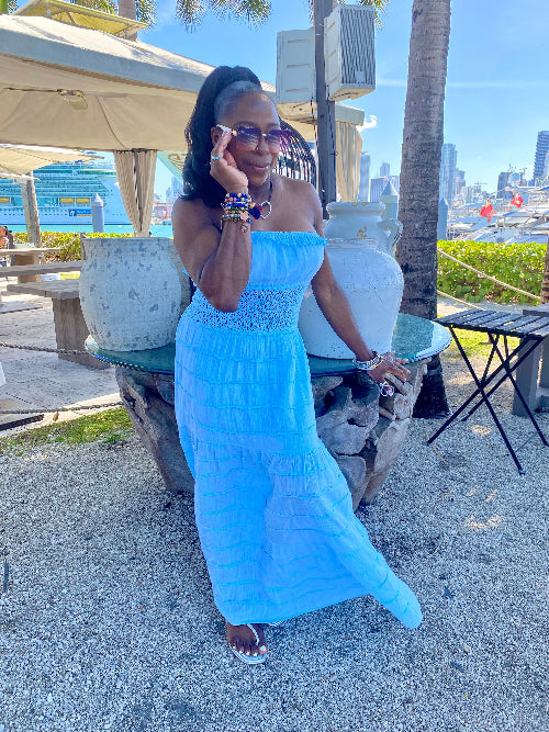Woman in a blue dress sitting outdoors with palm trees and city skyline in the background