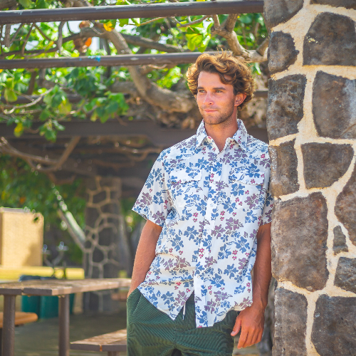 Man in a floral shirt leaning against a stone wall outdoors