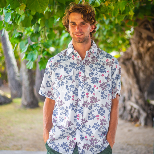 Man wearing a floral shirt standing in a natural setting with trees.