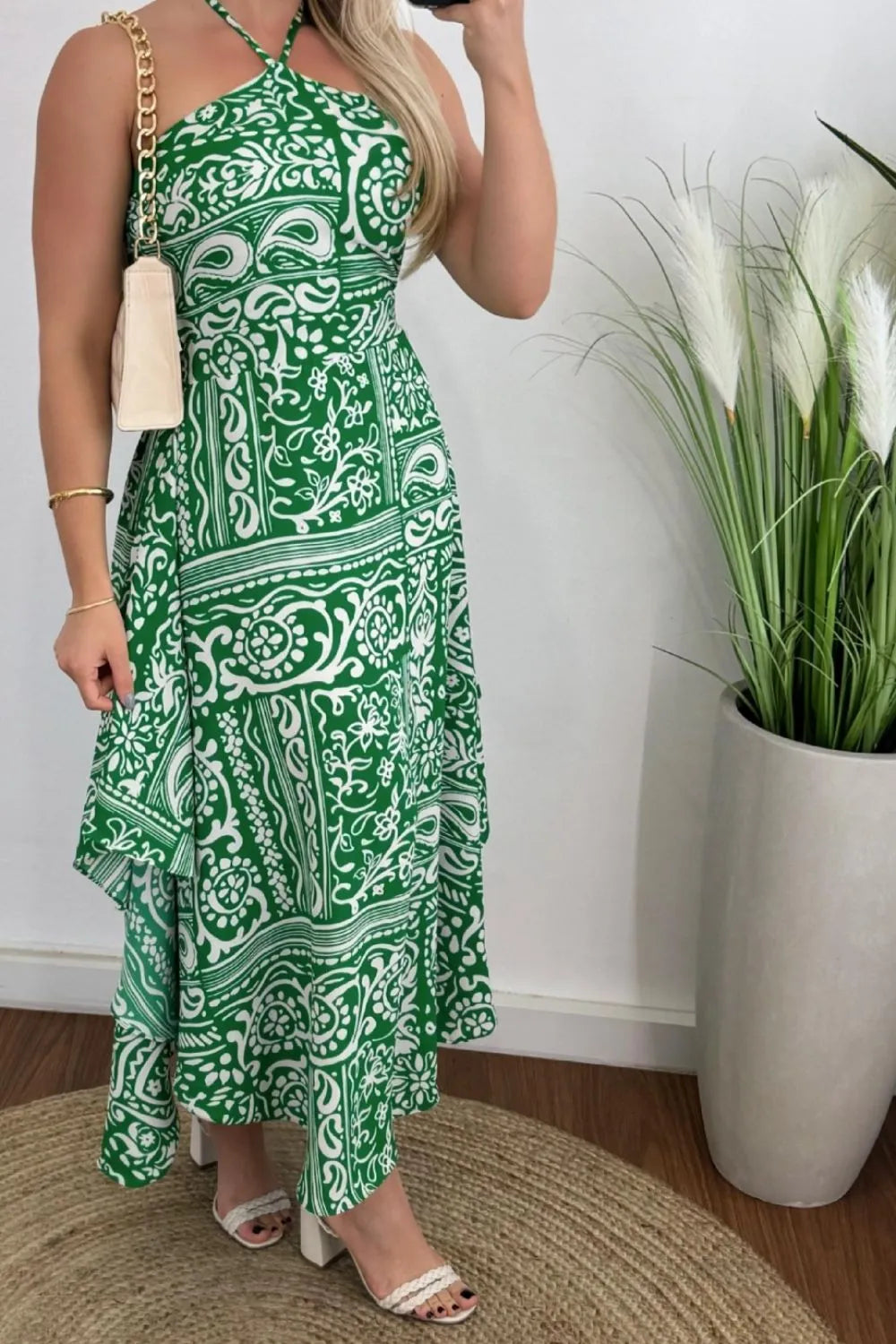 A model wearing a black halter neck dress with a printed floral pattern, paired with white accessories.