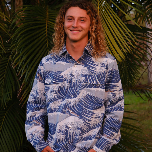 Person wearing a blue wave pattern shirt standing in front of green foliage