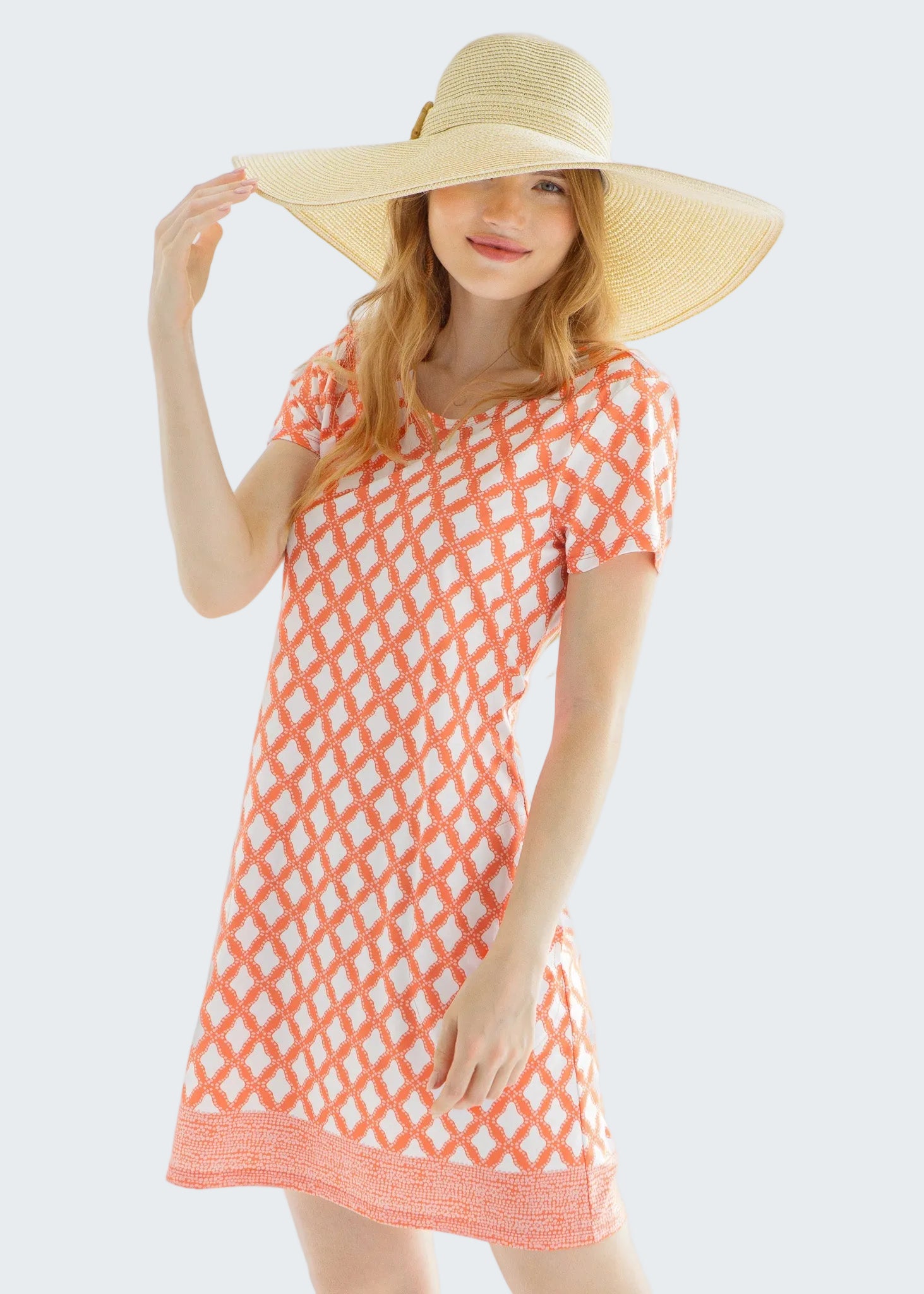 Woman wearing a coral patterned dress and wide-brimmed hat against a white background